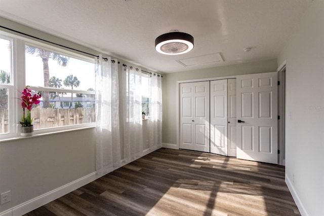 unfurnished bedroom featuring a closet, baseboards, attic access, and wood finished floors