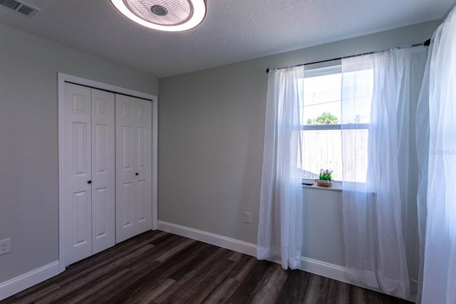 unfurnished bedroom featuring visible vents, baseboards, a textured ceiling, and dark wood-style floors