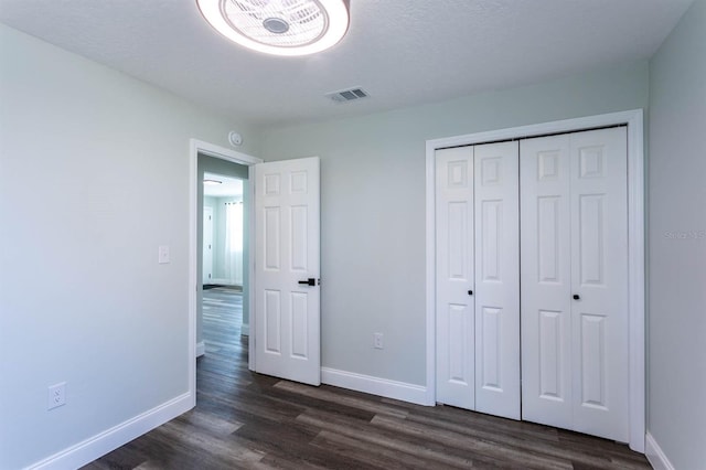 unfurnished bedroom with visible vents, baseboards, a closet, and dark wood-style floors
