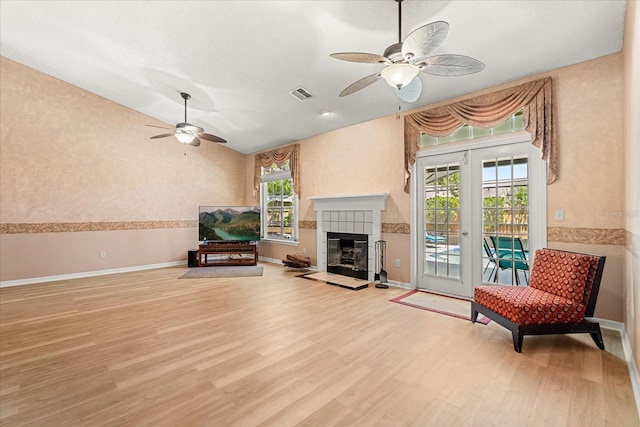 living area featuring wood finished floors, ceiling fan, a fireplace, baseboards, and visible vents