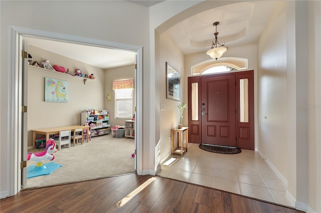 foyer with arched walkways, light wood finished floors, and baseboards