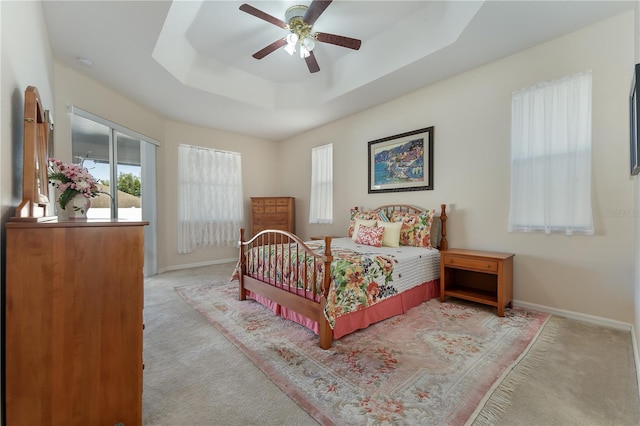 carpeted bedroom with ceiling fan, baseboards, and a raised ceiling