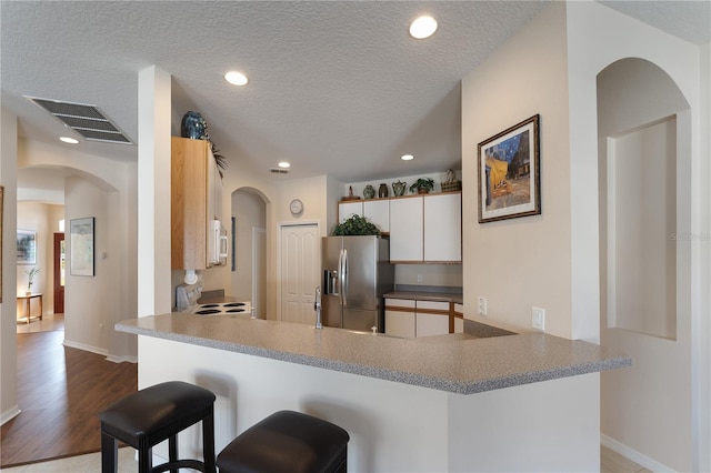 kitchen featuring a peninsula, arched walkways, visible vents, white appliances, and a breakfast bar area