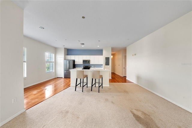 kitchen with white cabinets, stainless steel appliances, electric panel, baseboards, and light colored carpet