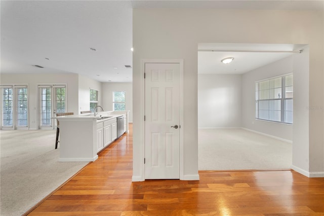 corridor with light colored carpet, light wood-style floors, baseboards, and a sink