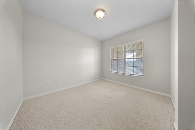 empty room featuring light carpet, vaulted ceiling, and baseboards