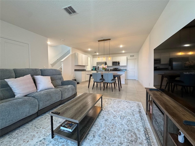 living room with stairs, light tile patterned floors, visible vents, and a textured ceiling