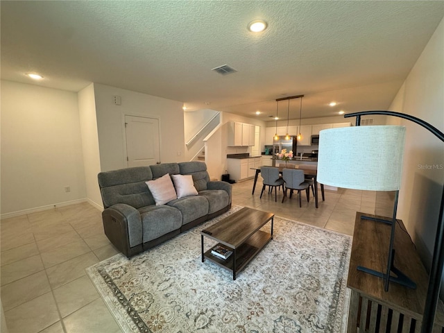living room featuring visible vents, baseboards, a textured ceiling, stairway, and light tile patterned flooring