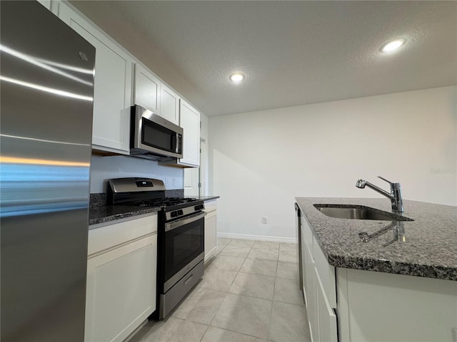 kitchen featuring baseboards, a sink, a textured ceiling, dark stone counters, and stainless steel appliances