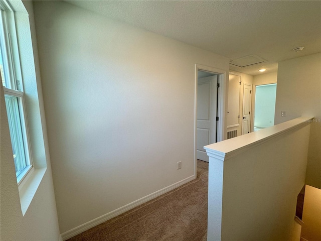 corridor with an upstairs landing, baseboards, a textured ceiling, and carpet floors
