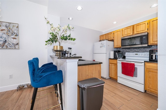 4011 Venetian Bay Dr Unit 103, Kissimmee, FL 34741 - kitchen featuring a breakfast bar, white appliances, backsplash, dark countertops, and light wood-style floors