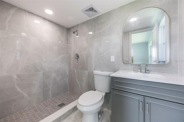 full bath with a tile shower, tile walls, toilet, visible vents, and vanity