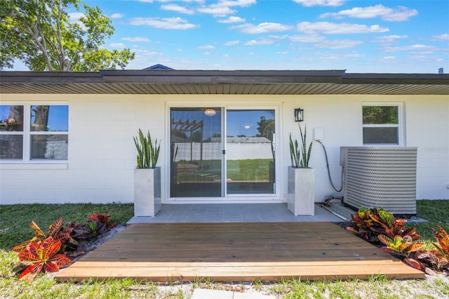 doorway to property with central AC unit, concrete block siding, and a wooden deck