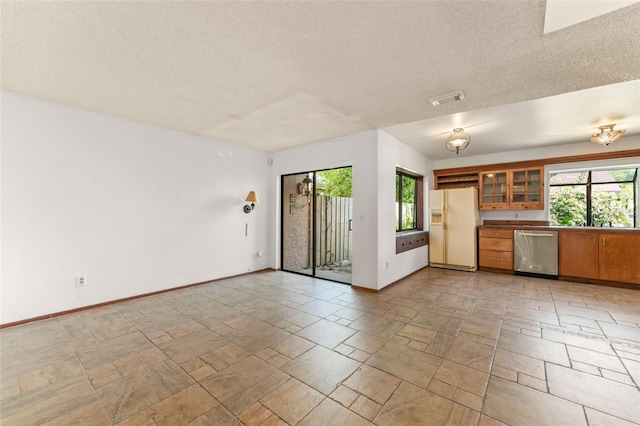 unfurnished living room featuring a textured ceiling, a sink, stone finish flooring, baseboards, and visible vents