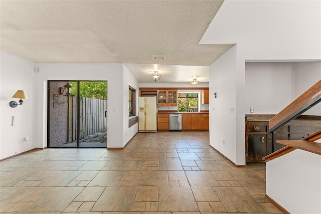 kitchen with stone tile floors, a wealth of natural light, white refrigerator with ice dispenser, and stainless steel dishwasher