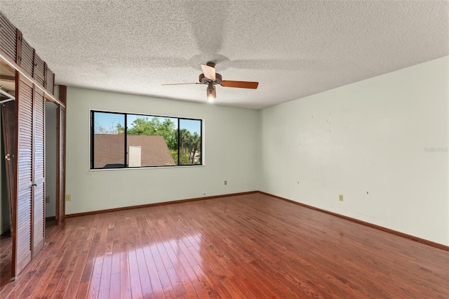 unfurnished bedroom featuring a textured ceiling, baseboards, a ceiling fan, hardwood / wood-style floors, and multiple closets