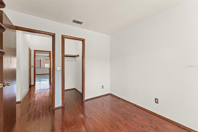 unfurnished bedroom featuring a textured ceiling, baseboards, visible vents, a closet, and hardwood / wood-style floors