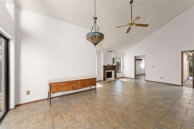 unfurnished living room featuring high vaulted ceiling, stone tile floors, ceiling fan, a fireplace, and baseboards