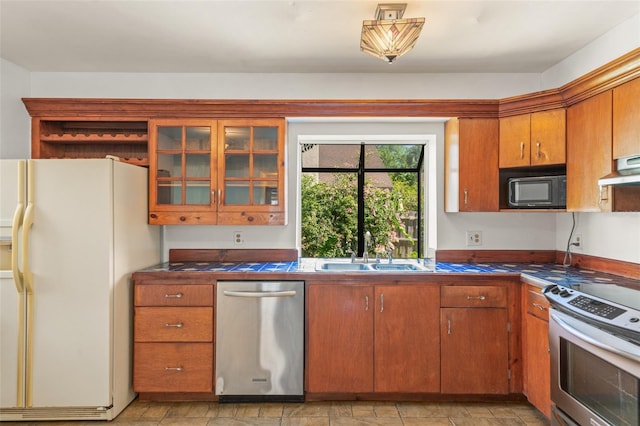 kitchen featuring a sink, glass insert cabinets, brown cabinets, under cabinet range hood, and appliances with stainless steel finishes