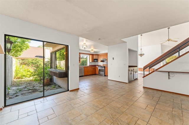 unfurnished living room featuring ceiling fan, baseboards, stone finish floor, and stairs