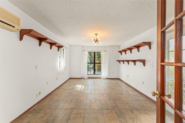 empty room with baseboards, stone finish floor, a textured ceiling, and a wall unit AC