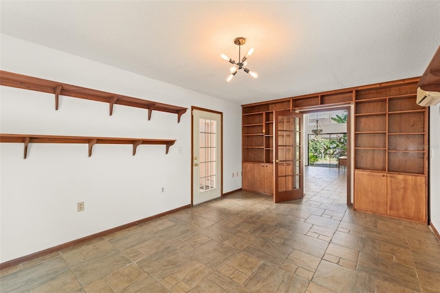 unfurnished room with french doors, stone tile floors, baseboards, built in features, and a notable chandelier