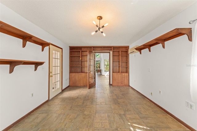 empty room featuring french doors, baseboards, built in features, an inviting chandelier, and stone finish flooring