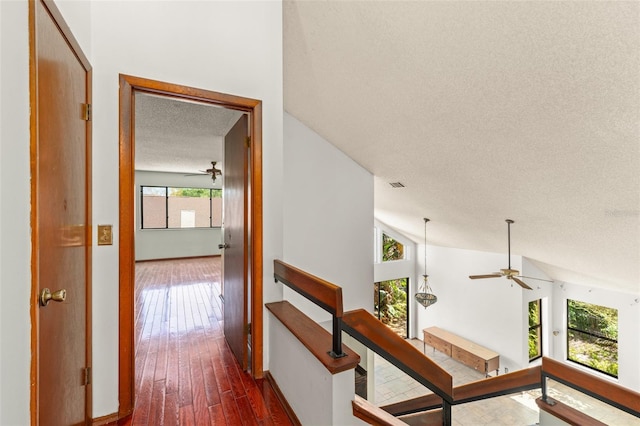 corridor with vaulted ceiling, a textured ceiling, dark wood finished floors, baseboards, and visible vents