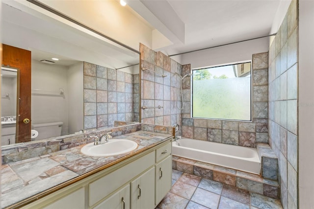 bathroom with stone tile floors, vanity, tiled shower / bath combo, and toilet