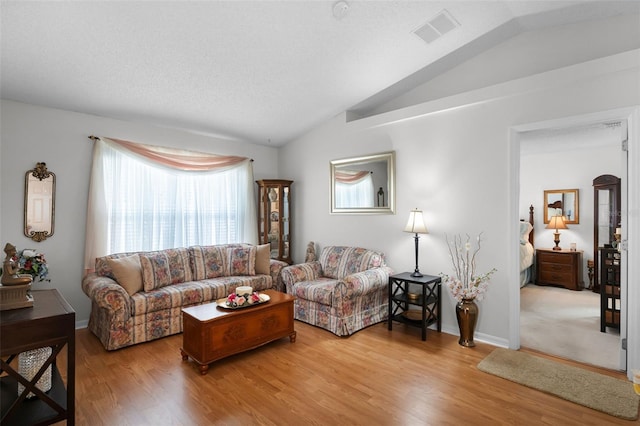 living area with visible vents, light wood-style flooring, and lofted ceiling