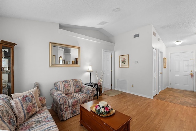 living area featuring light wood-style flooring, vaulted ceiling, a textured ceiling, and visible vents