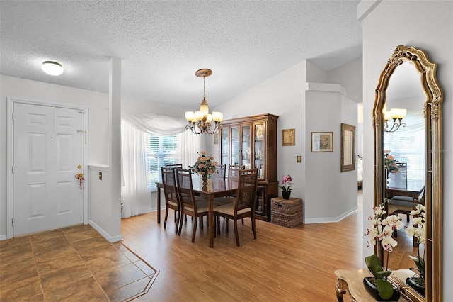 dining room with an inviting chandelier, light wood finished floors, a textured ceiling, baseboards, and lofted ceiling