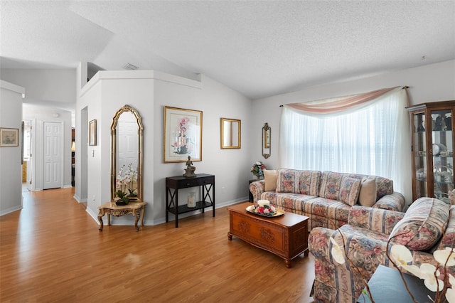 living area with light wood-style floors, a textured ceiling, vaulted ceiling, and visible vents