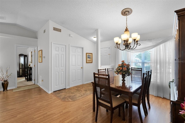 dining area with a notable chandelier, light wood-style floors, a textured ceiling, lofted ceiling, and visible vents
