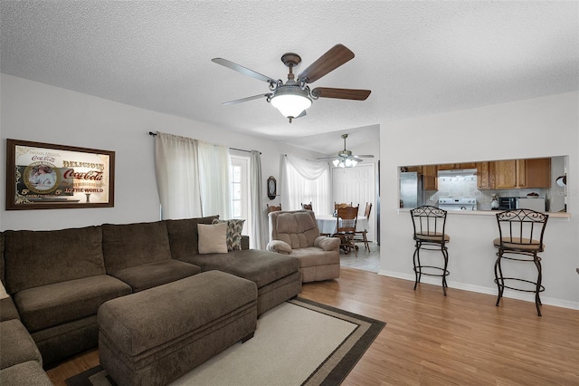 living area featuring light wood-style floors, baseboards, ceiling fan, and a textured ceiling