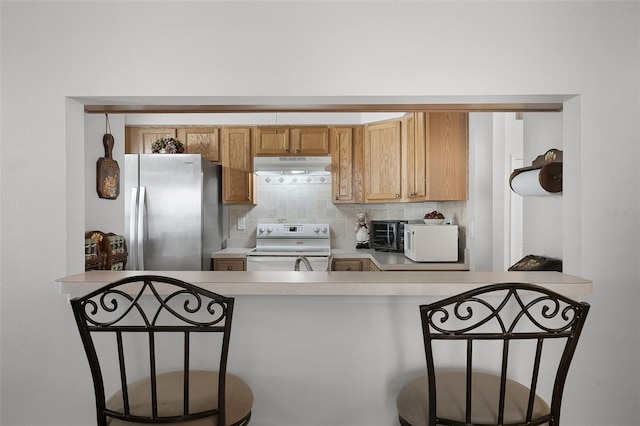 kitchen with under cabinet range hood, decorative backsplash, white appliances, and light countertops