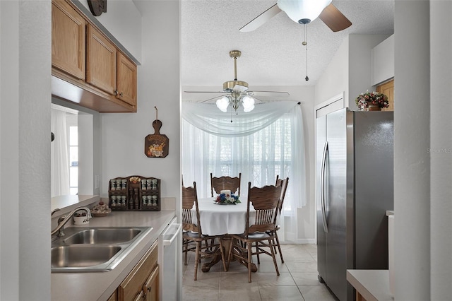 kitchen featuring brown cabinets, a sink, dishwasher, freestanding refrigerator, and a ceiling fan