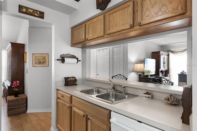 kitchen with dishwasher, a sink, light countertops, baseboards, and light wood-style floors