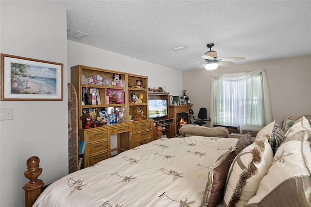 bedroom with a lit fireplace, a ceiling fan, a textured ceiling, and visible vents