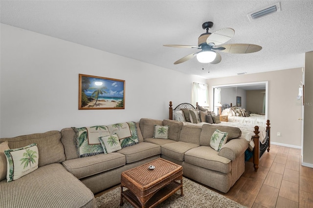 living room with ceiling fan, a textured ceiling, visible vents, wood finished floors, and baseboards