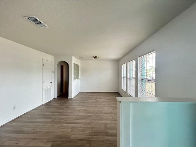 spare room featuring dark wood-style floors, arched walkways, visible vents, and baseboards