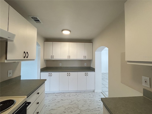 kitchen with marble finish floor, dark countertops, visible vents, arched walkways, and white cabinetry