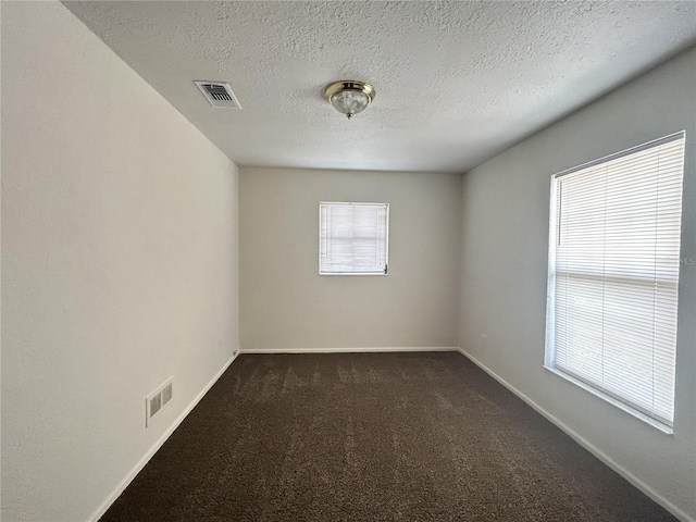empty room with baseboards, dark colored carpet, a textured ceiling, and visible vents