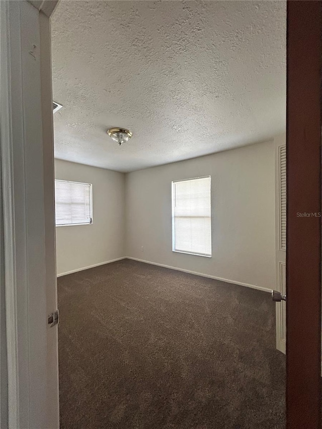 empty room featuring dark colored carpet, a textured ceiling, and baseboards