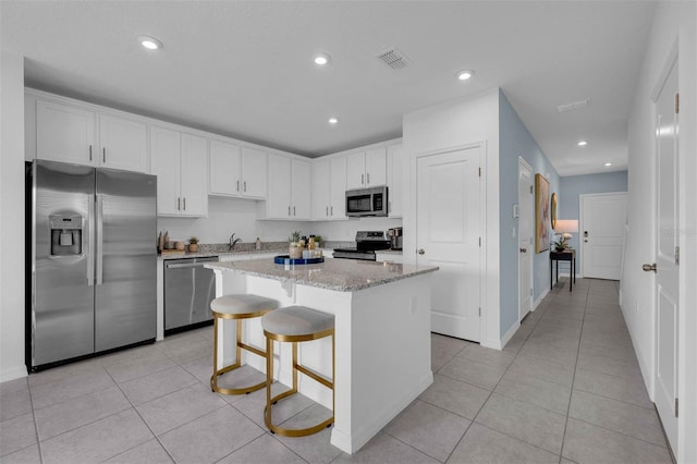 1409 Fan Palm Dr, Davenport, FL 33897 - kitchen with light stone counters, light tile patterned floors, a kitchen island, visible vents, and appliances with stainless steel finishes