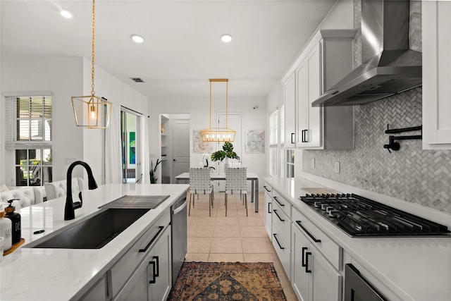 kitchen with a sink, light tile patterned floors, backsplash, wall chimney exhaust hood, and appliances with stainless steel finishes