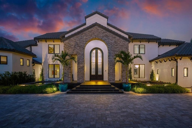 570 Manor Rd, Maitland, FL 32751 - exterior entry at dusk featuring stucco siding, stone siding, a tiled roof, and french doors