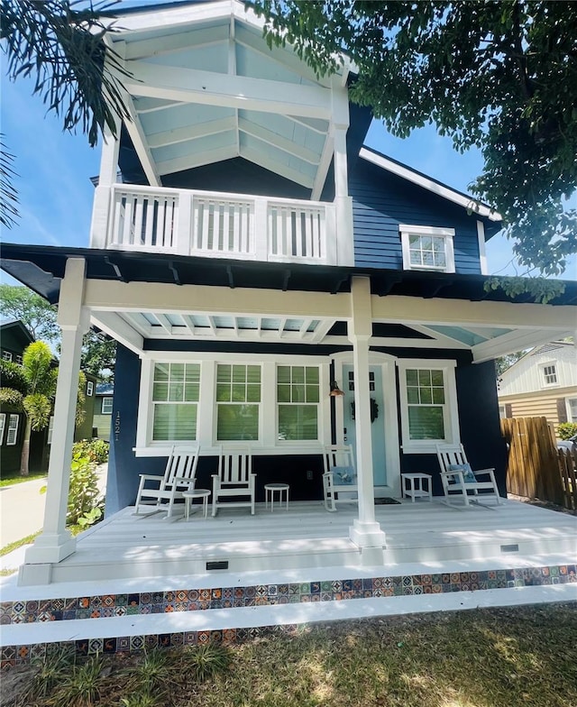 back of house featuring covered porch, a balcony, and fence