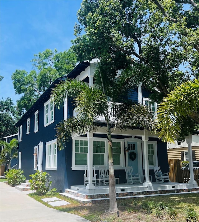 view of front of property featuring a porch, stucco siding, and fence