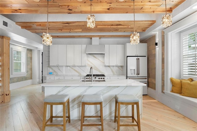 kitchen featuring high end white fridge, a chandelier, wall chimney range hood, a kitchen breakfast bar, and beam ceiling